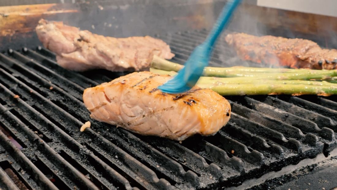 Salmon, steaks and asparagus cooking on the grill line in the Steak & Take kitchen