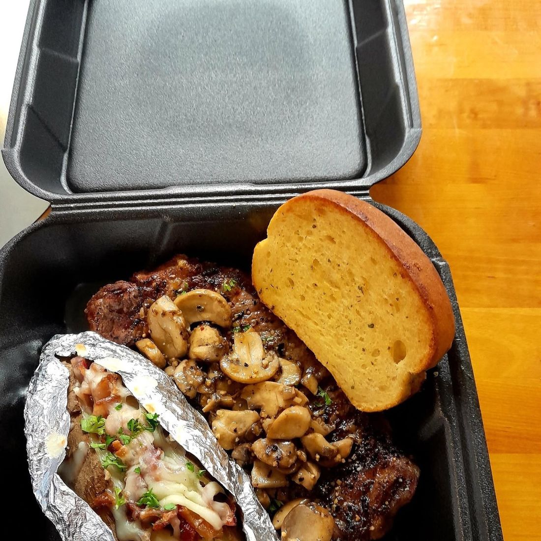 Grilled ribeye topped with sauteed mushrooms, with a loaded baked potato and garlic bread