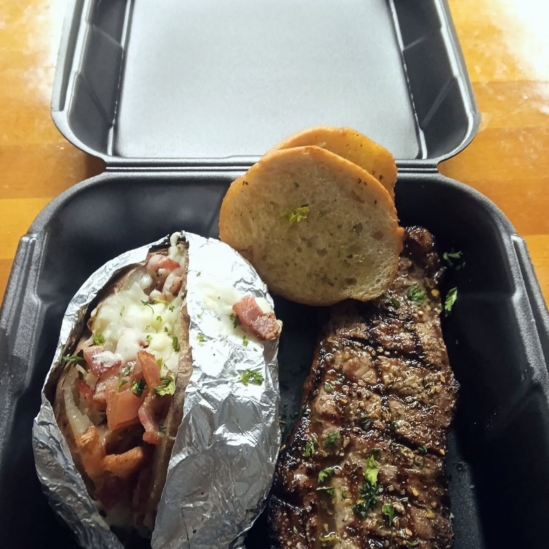 Grilled steak with a loaded baked potato and garlic bread, packed to go